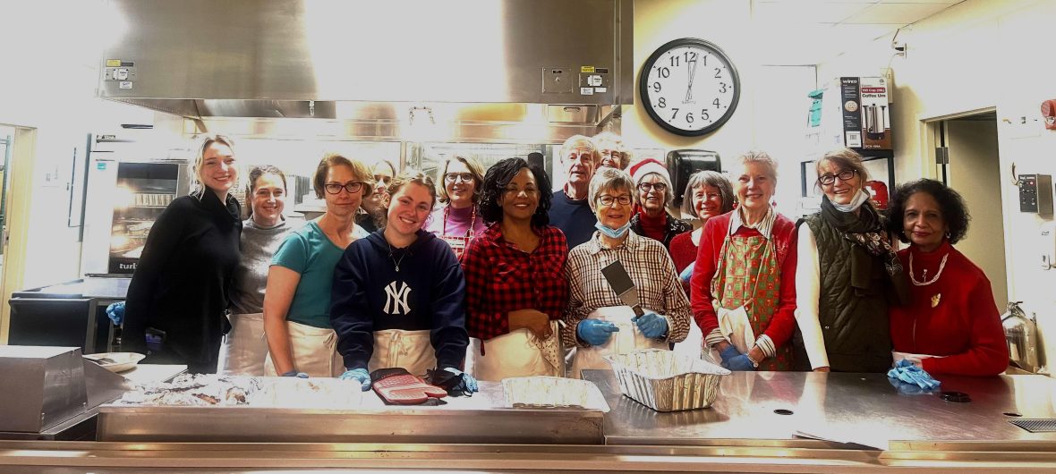 Group of volunteers standing in a kitchen behind the counter smiling at the camera
